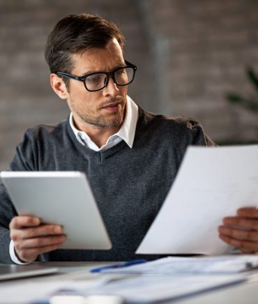 Businessman reading reports and using touchpad while working in the office.